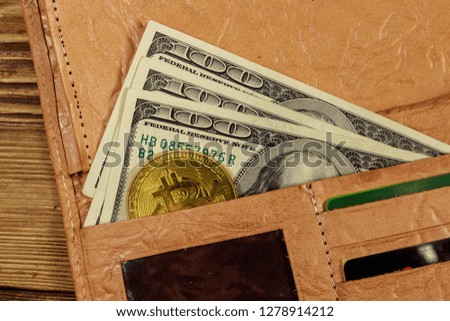 Wallet with american hundred dollars bills and golden bitcoin on wooden background