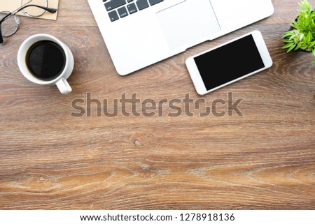 Wood desk table with smartphone with blank mock up screen, laptop computer and up of coffee with sun light in the morning. Top view with copy space, flat lay.