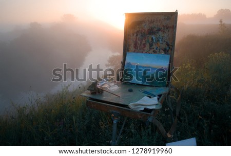 The artist paints a picture outdoors in the early summer morning. Painting in nature. Fine art. Artist, sketch, etude. pattern. Foggy landscape. Misty summer morning