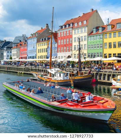 Tourists sightseeing cruising on boat by Nyhavn embankment with bars and restaurants in buildings of old architecture, Copenhagen, Denmark 