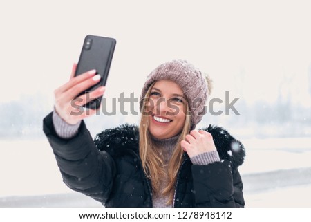 Smiling woman taking selfie outdoors.