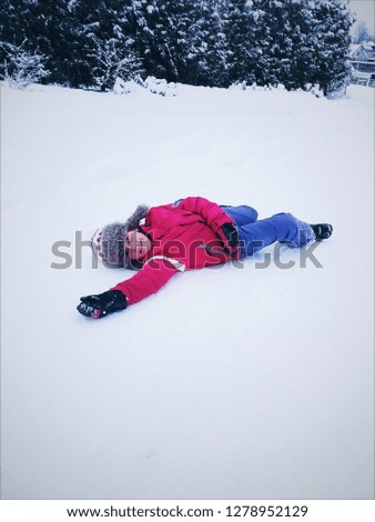 little cute girl in winter fur hat and sportswear, warm clothes, on a winter day, lying down and resting in the snow, after winter fun games