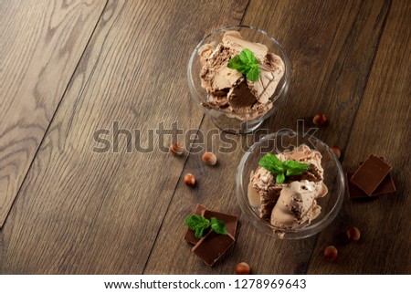 Homemade chocolate ice cream with mint leaves, sprinkled with chocolate in a glass bowl on a wooden table. chocolate pieces, hazelnuts. Selective focus, copy space.