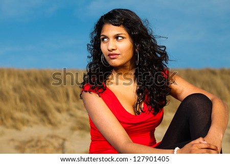 Indian girl with long hair dressed in red on the beach in summer.