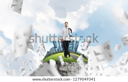 Confident young businessman in suit standing on flying island with huge white banner in hands which pointing away and with cloudy skyscape on background