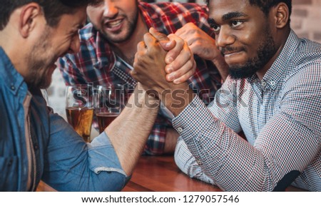 Male friends arm wrestling each other, drinking beer in bar
