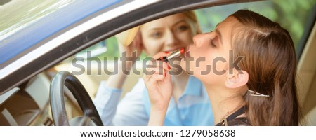 Drive safely. Pretty woman applying red lipstick on lips. Young woman with perfect makeup at car wheel. Fashion model with glossy lip makeup. Beauty look of glamour model. Visage and makeup.