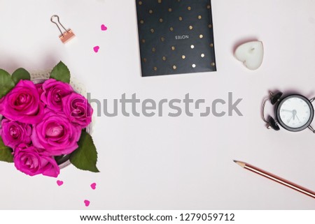 Creative frame with roses,notepad, small paper hearts and other small items on pastel pink background.