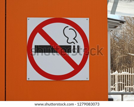   Sign - no smoking, attached to the orange wall on the street.        