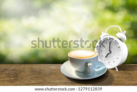 A cup of hot coffee with an alarm clock placed on a wooden table .And a natural background bokeh with copy space for your message. Coffee time concept in the morning