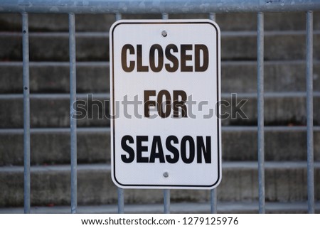 White sign closed for season on gray metal fence closeup
