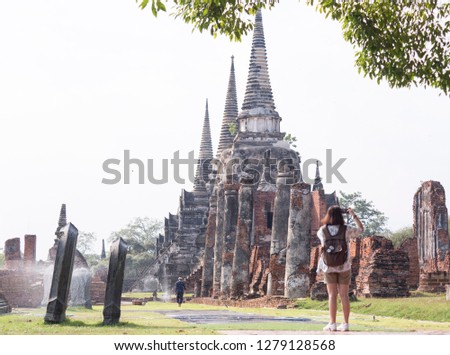 A thai asian woman wear a white shirt and short and have a big bag stand alone and take a photo in the temple.