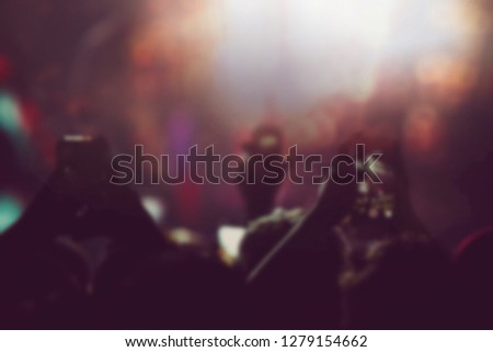 Blurry background with music fans filming concert with smartphone in bright stage lights. Festival audience take pictures with mobile phone cameras on entertainment event in night club