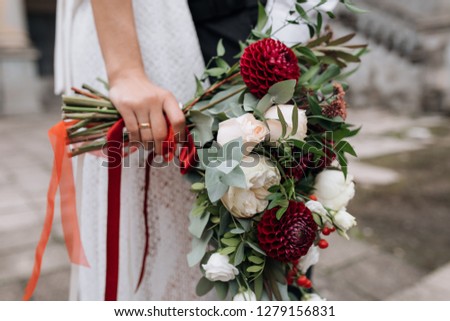 Bride in white dress holds rich bouquet of red and white flowers