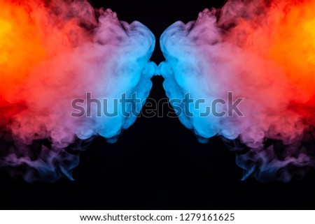 Soaring thick colorful smoke iridescent like a rainbow in bright colors divided into two halves on a black background swirling in waves.
