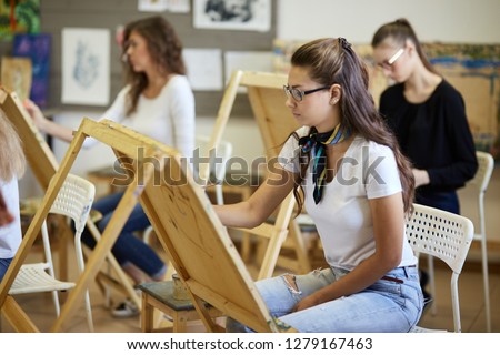Drawing lesson in the art studio. Tree charming young girls paint pictures sitting at the easels