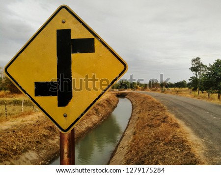 Close-up view of old Intersection sign,background waterway,small road,cornfield and Blue sky,When having to find the intersection of life, going left or right, going forward or turning back.