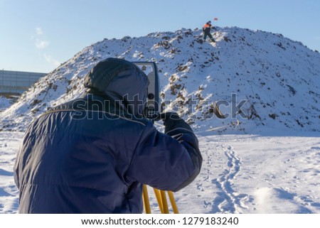 Surveyor and assistant conduct a topographical survey in the winter for cadastral work