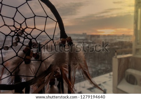 Handmade dreamcatcher hanging by the window with blinds in sunset twilight. Black silhouette of traditional magic amulet for dream protection and bad spirits.