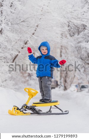 funny boy standing on a snow scooter in winter