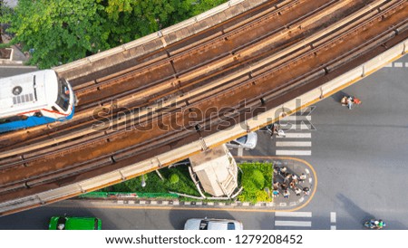 Top view aerial of a driving car on asphalt track and pedestrian crosswalk in traffic road  with sky train run on the top rail.