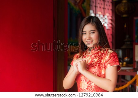 Portrait images of Chinese girl Wearing a red Cheongsam dress Made a gesture of blessing on the Chinese New Year with red wall background.