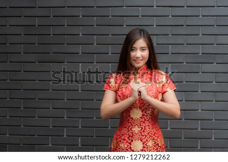 Portrait images of Chinese girl Wearing a red Cheongsam dress Made a gesture of blessing on the Chinese New Year with black wall background.