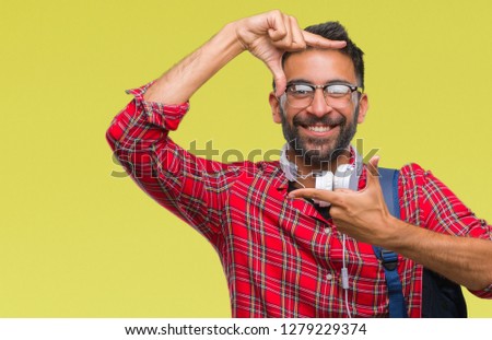 Adult hispanic student man wearing headphones and backpack over isolated background smiling making frame with hands and fingers with happy face. Creativity and photography concept.