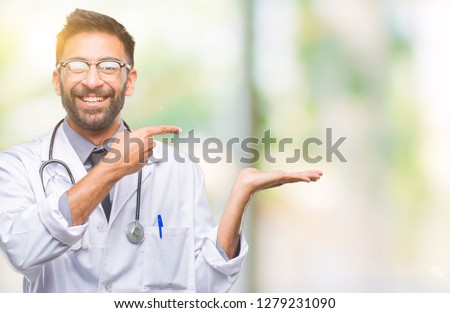 Adult hispanic doctor man over isolated background amazed and smiling to the camera while presenting with hand and pointing with finger.