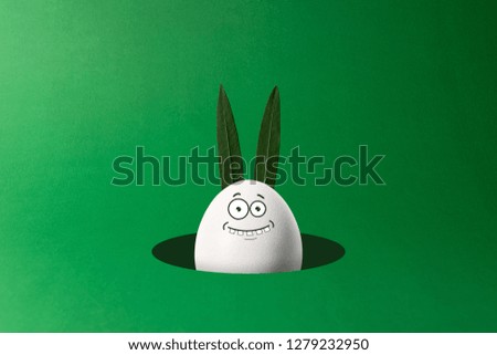 Easter egg with bunny ears and funny face peeking out from hole. Minimal concept.