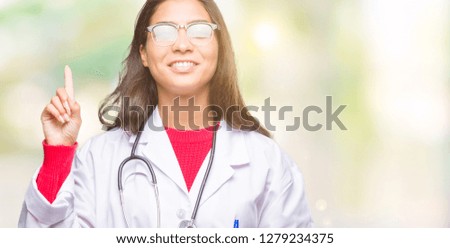Young arab doctor woman over isolated background showing and pointing up with finger number one while smiling confident and happy.