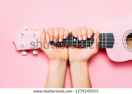 Woman hand with fashion manicure holding little pink ukulele on pink background. Fine female musician picture. Top view, flat lay.