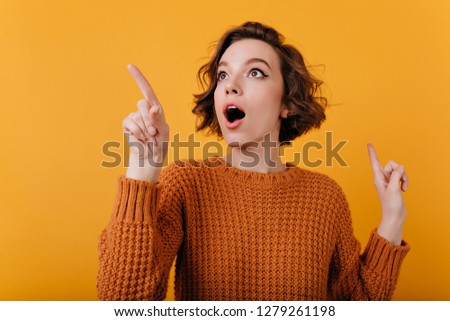 Close-up portrait of enthusiastic girl with suprised face expression looking around. Studio shot of lovable curly lady isolated on orange background. Royalty-Free Stock Photo #1279261198