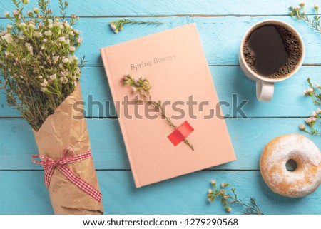 Breakfast on a blue table with hot coffee and donut. Pink notebook and a spring flowers bouquet