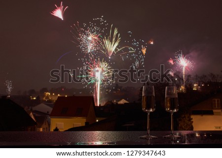 horizontal color picture of two glasses with sparkling wine, in the background blurred fireworks