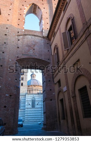 Europe, Italy, Siena. Narrow street in historic city center early morning. Dome of cathedral framed in archway