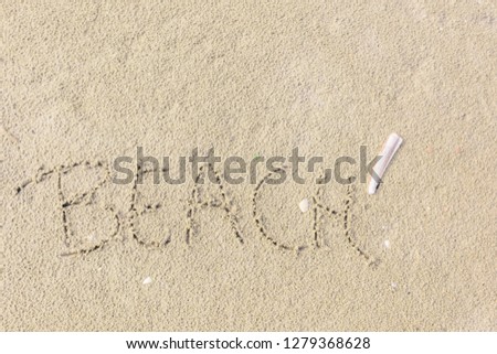 The word "Beach" is written in the sand as a concept of freedom, relaxation and vacation. A razor clam (ensis ensis) lies next to the word in the sand.