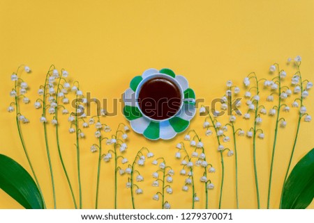 Lilies of the valley flowers and tea cup on bright yellow paper background. Beautiful spring composition in minimal style. Top view, flat lay, copy space