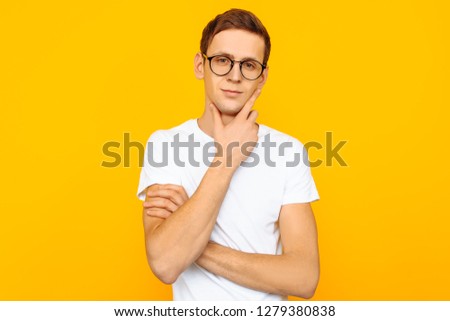 Cute guy in glasses, dressed in a white T-shirt, posing on a yellow background