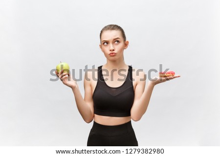 Young woman choosing between donut and apple on white background. Diet food concept