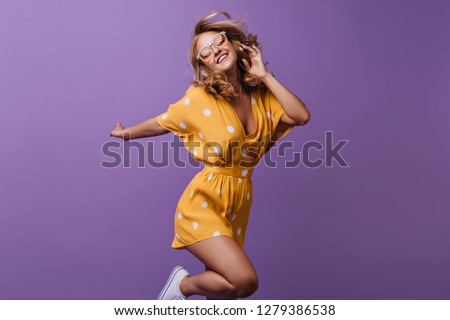 Stunning curly female model jumping on purple background. Indoor photo of slim girl in bright yellow dress.