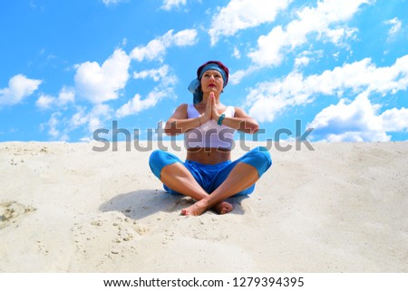 An old woman sitting on the sand in the desert in a Lotus position. Yoga, exercise
