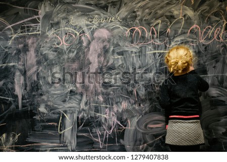 child draws with chalk on a blackboard