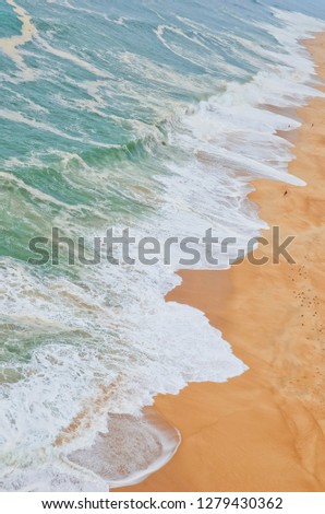 Amazing aerial view of waves washing up on sandy beach in portuguese Nazaré taken during summer season. On the beach there is flock of seagulls and several persons chilling out or taking photos.  