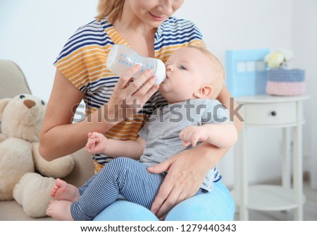 Lovely mother feeding her baby from bottle in room at home