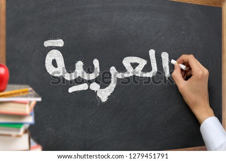 Hand writing on a blackboard in a 
Arabic language learning class course with the text "Arabic" written on it. with Some books and school materials concept.
