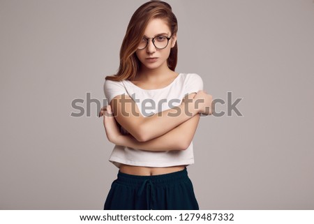 Portrait of cute teenage girl in white shirt and glasses posing on gray background. Studio shoot.