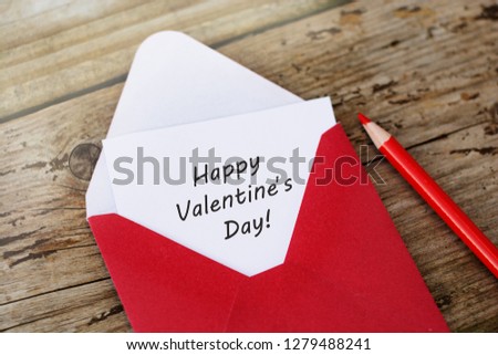 Happy Valentine's Day inscription - red envelope with blank card on wooden background with copy space, and red pencils.