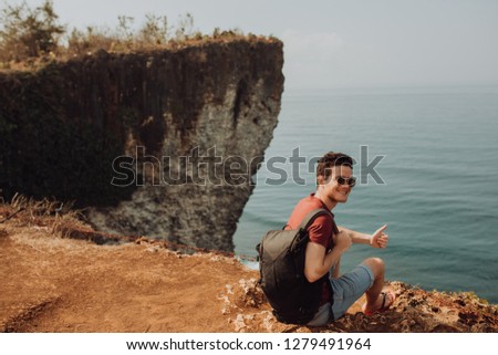 Young man using a backpack on top a ocean cliff, happy smiling emotions