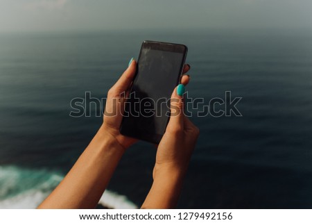 girl holding a smartphone mobile phone on the edge of the cliff near the ocean.